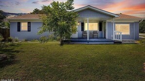 Una casa de un piso con un porche cubierto, un pequeño jardín y un árbol en la parte delantera.