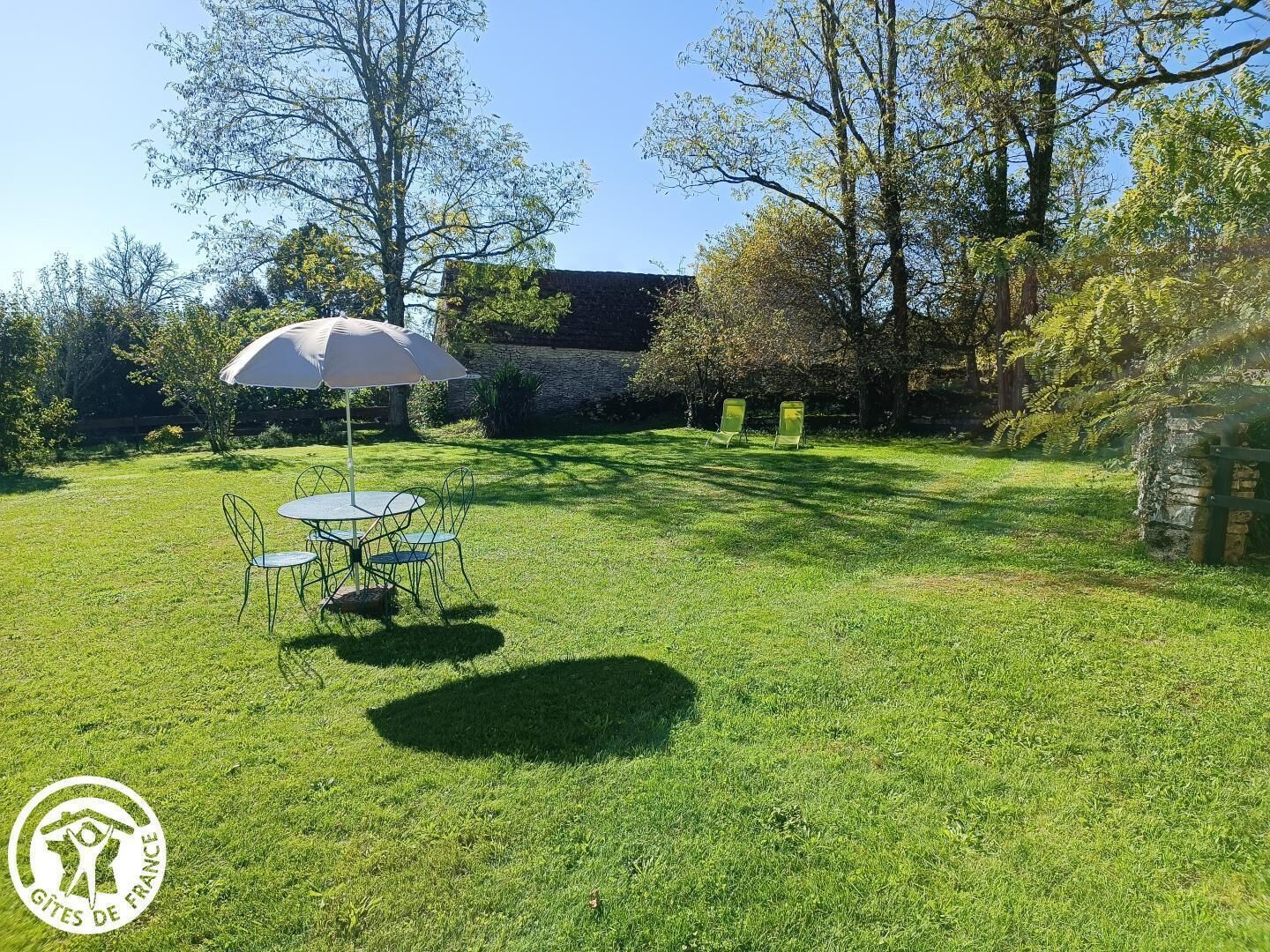 A grassy outdoor area with a table and chairs, an umbrella, and a stone wall.
