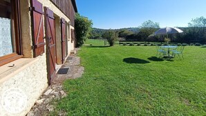A rustic barn with wooden shutters and a grassy yard. - Gîtes de France® - Le Fenil (ROCAMADOUR)