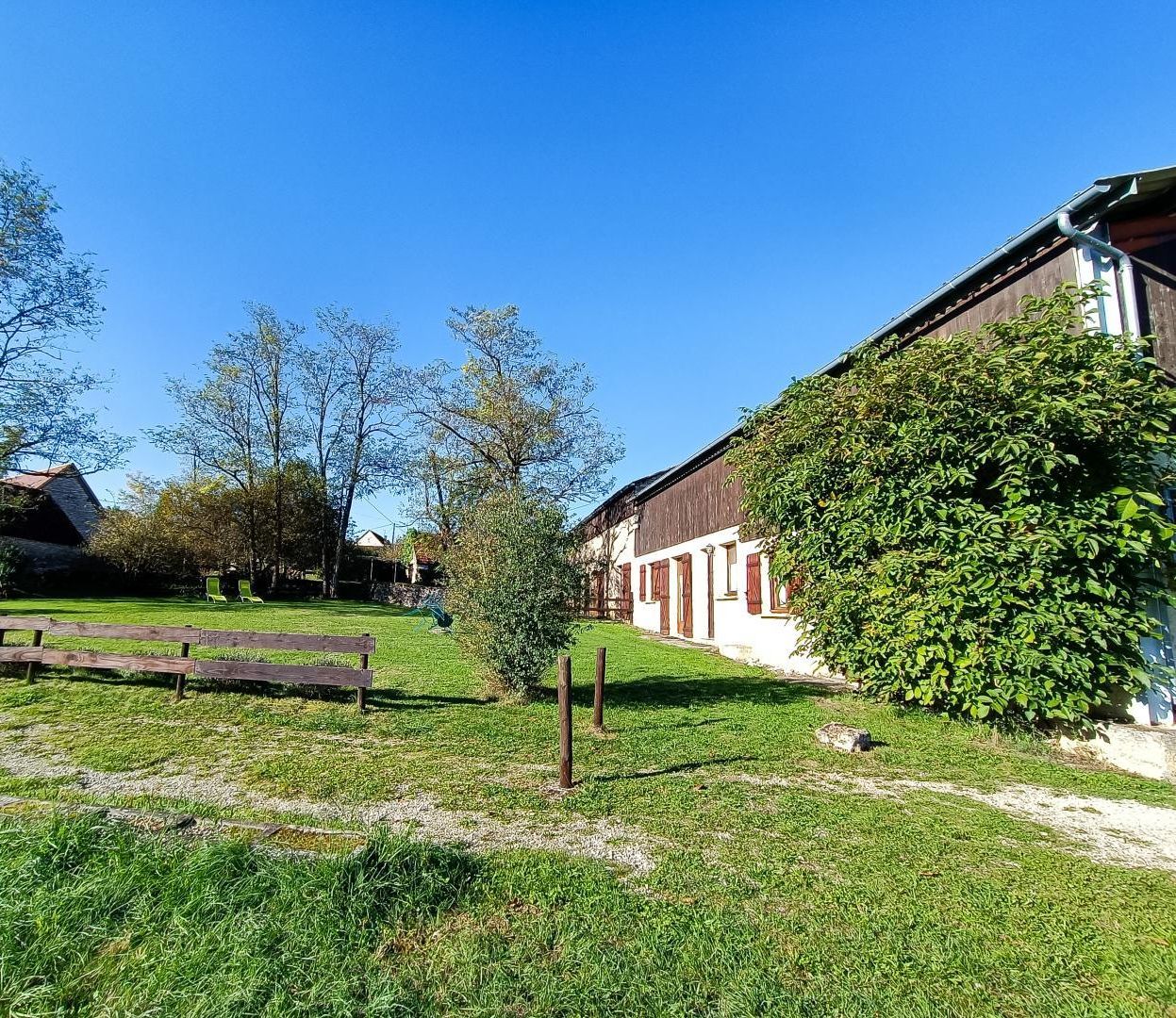 Une propriété rurale dotée d’une pelouse verdoyante, d’une clôture en bois et d’un bâtiment aux volets rouges.