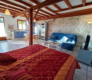 Un dormitorio con una cama grande, pared de piedra, sofá azul y una zona de cocina al fondo.