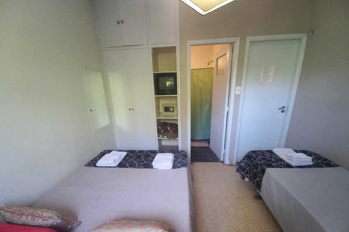 A small, compact room with two single beds, a wardrobe, and a shower area.