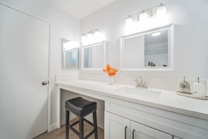 A bathroom with a white vanity, a black stool, a mirror with lights, and a vase with orange flowers. - 2 TVs  Vaulted Ceiling  Private Kitchen&Entrance (Walnut)