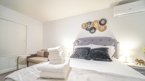 Cama bem arrumada com roupa de cama branca, cabeceira estofada cinza e uma obra de arte decorativa acima.
