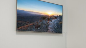 Quarto com uma grande pintura de paisagem na parede, uma mesa consola de madeira e uma cama com cabeceira branca.