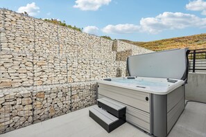 Un jacuzzi con escalones, frente a una pared de piedra, en el exterior.