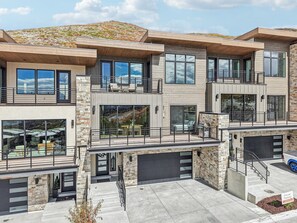 Un edificio residencial moderno de varios pisos con fachada de piedra, ventanas grandes y un área de estar al aire libre techada.