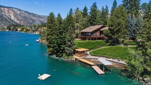 A lakeside property with a wooden dock, a covered seating area, and a large house with a balcony overlooking the water. - Armstrong Lake House (Manson)