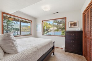 A bedroom with a bed, two windows with views of nature, a dresser, and a framed picture on the wall.