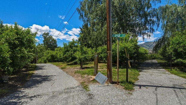 A gravel road with a green street sign, surrounded by lush greenery and trees. - Armstrong Lake House (Manson)