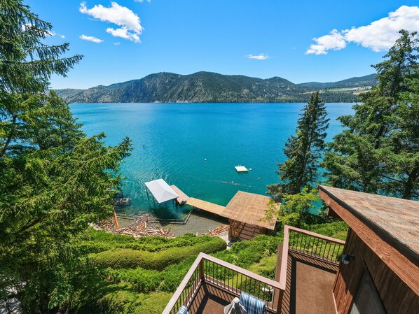 A lakeside view with a dock, wooden deck, and lush greenery.