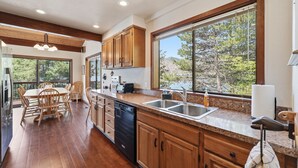 Una cucina moderna con mobili in legno, un piano di lavoro in granito, una lavastoviglie e un'ampia finestra vista alberi.