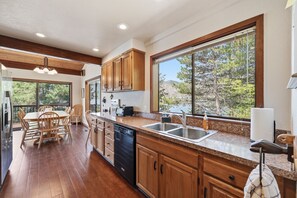 Une cuisine moderne avec des meubles en bois, un plan de travail en granit, un lave-vaisselle et une grande fenêtre donnant sur la forêt.