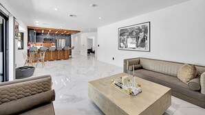A modern living room with a sofa, a coffee table, and a dining area in the background. - HOUSE OF PRINCE – Luxury 4BR Palm Springs retreat with pool, gym & kids’ room. (Palm Springs)
