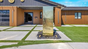 A modern building with a large central pillar, a garage, and a well-maintained lawn. - HOUSE OF PRINCE – Luxury 4BR Palm Springs retreat with pool, gym & kids’ room. (Palm Springs)