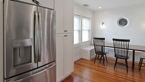A kitchen with a stainless steel refrigerator, white cabinetry, a dining table with chairs, and a window with blinds. - Charming Bradenton getaway on the Gulf Coast - Flip Flop Retreat (Bradenton)