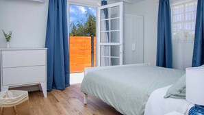 Un dormitori amb un llit, una petita taula de nit, una finestra amb cortines i una tanca de fusta a l'exterior.