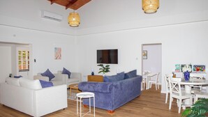 A modern living room with a white sofa, a blue sofa, and a coffee table. There is a TV mounted on the wall and a small table with a plant. - Hello Summer! 2BR Home w/ Pool, 5min Walk to Reduit Beach, Dining & Nightlife in Rodney Bay! (Rodney Bay)