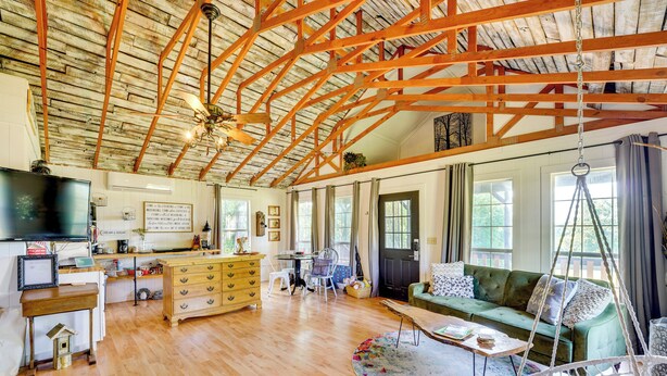A spacious living room with a wooden ceiling, a green sofa, a hanging chair, and a dining area with a table and chairs. - 1 Mi to Downtown Eureka Springs: Studio Retreat (Eureka Springs)