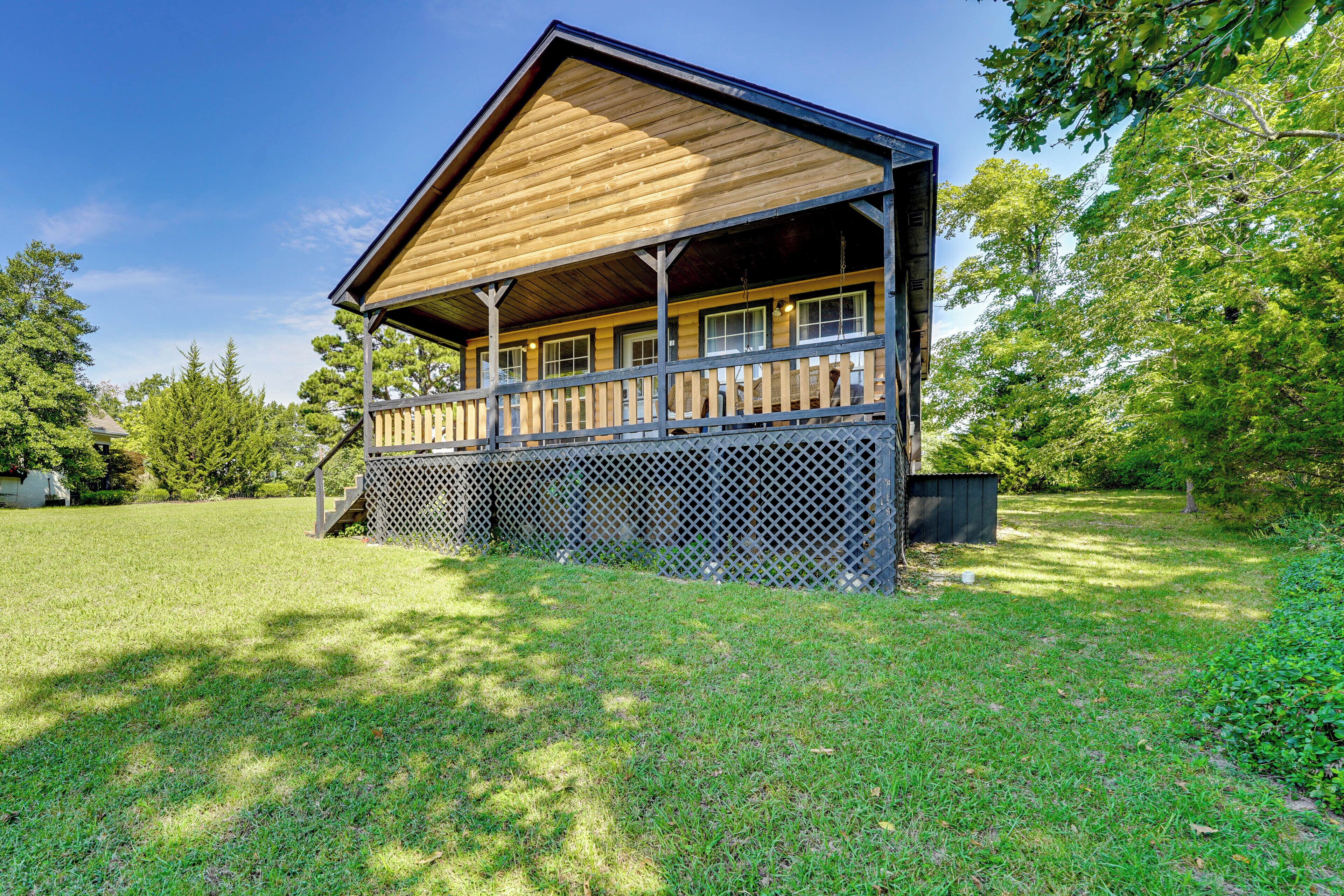 A wooden cabin with a porch, surrounded by a grassy yard and trees.