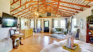 A spacious living room with wooden beams, a large TV, a sofa, and a dining area. - 1 Mi to Downtown Eureka Springs: Studio Retreat (Eureka Springs)