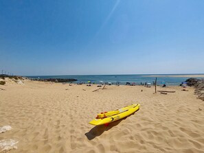 Ein sandiger Strand mit einem gelben Kajak und blauem, wolkenlosem Himmel.