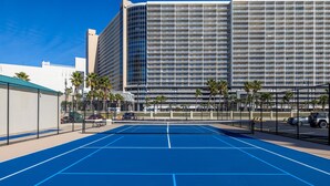 Un campo da tennis all'aperto accanto a un hotel, con un grattacielo sullo sfondo.