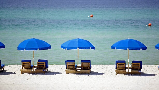 Una spiaggia con ombrelloni blu e lettini di legno.