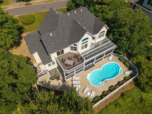 A two-story house with a large swimming pool, a covered patio, and a well-maintained lawn.