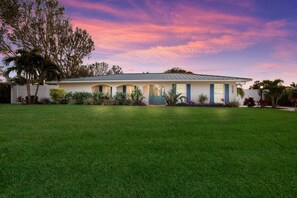 A single-story house with a front porch, a well-maintained lawn, and a clear sky. - Tropical Tiki:Outdoor Oasis, Tiki Hut, Pool by Anna Maria Life Vacation Rentals (Bradenton)