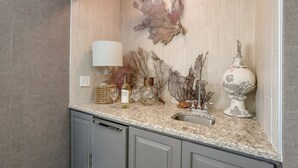 A kitchen with a marble countertop, a wine bottle, two wine glasses, a decorative vase, and a sink. - Tropical Tiki:Outdoor Oasis, Tiki Hut, Pool by Anna Maria Life Vacation Rentals (Bradenton)