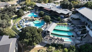 Vista aérea de un complejo turístico con múltiples piscinas, un edificio grande de techo plano y vegetación circundante.