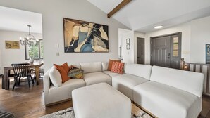 Een moderne woonkamer met een modulaire bank, een eethoek met een houten tafel en stoelen, en een groot abstract schilderij aan de muur.