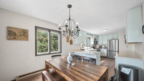 Een moderne keuken met een houten eettafel, een kroonluchter en roestvrijstalen apparatuur.