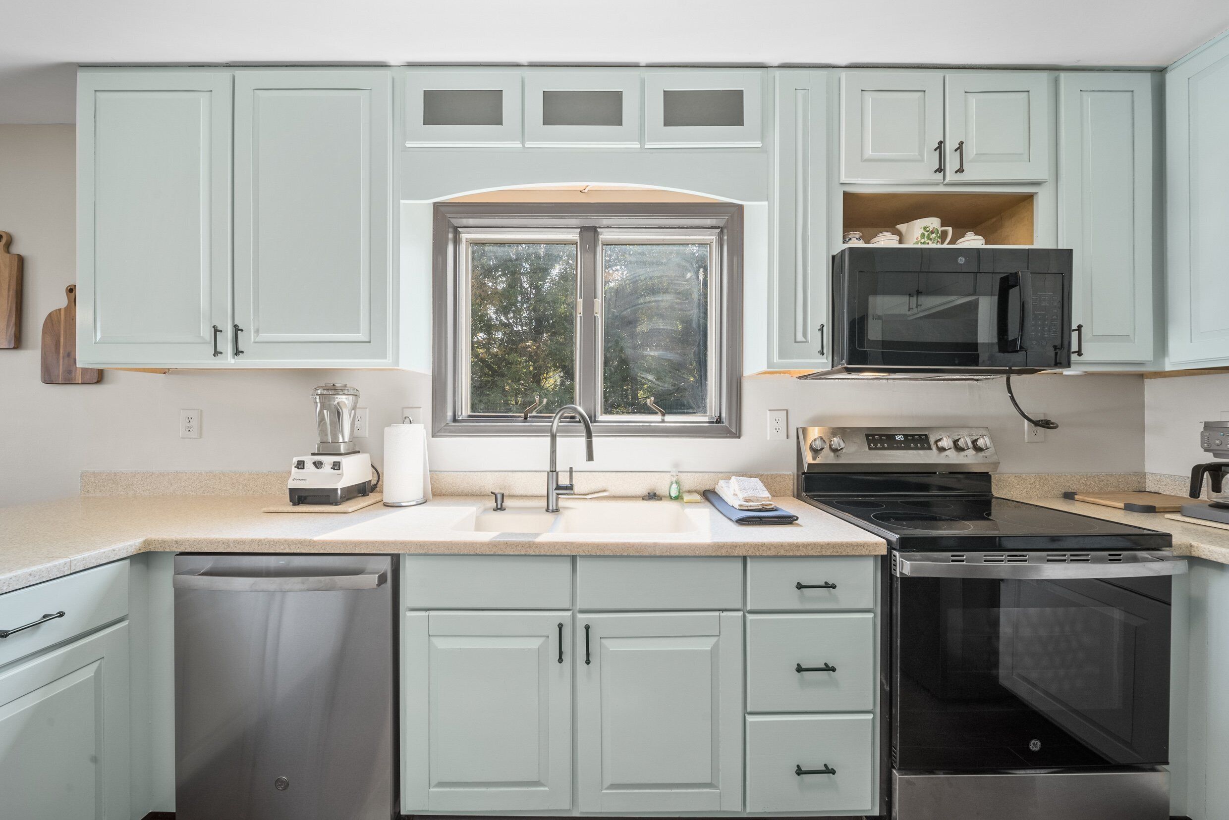 A modern kitchen with light green cabinets, a double sink, a built-in microwave, a stove, and a dishwasher.
