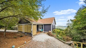 Een huis met een grindpad, houten omheining en uitzicht op een bebost gebied.
