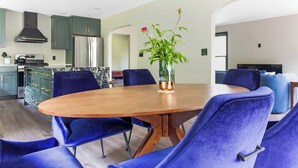 Una cocina moderna con armarios verdes, un refrigerador de acero inoxidable y una mesa de comedor de madera con sillas azules.