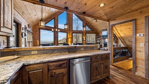 A kitchen with wooden cabinets, a stainless steel dishwasher, and large windows offering a view of the outdoors. - Grandeur View Lodge - Mountain View | Hot Tub | Game Room (Blue Ridge)