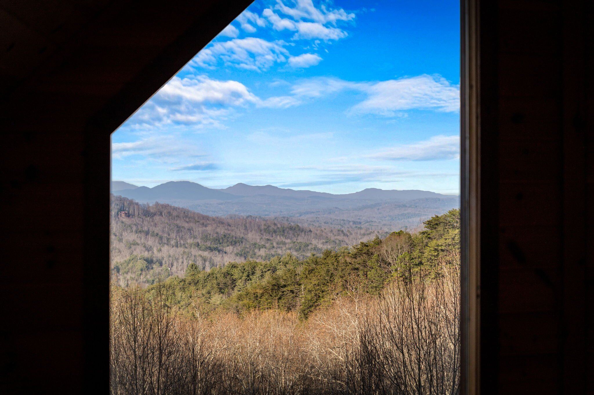 A view from a window overlooking a forested landscape with mountains in the distance.