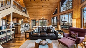 A spacious wooden interior with a high ceiling, a cozy seating area, and large windows offering views of the outdoors. - Grandeur View Lodge - Mountain View | Hot Tub | Game Room (Blue Ridge)