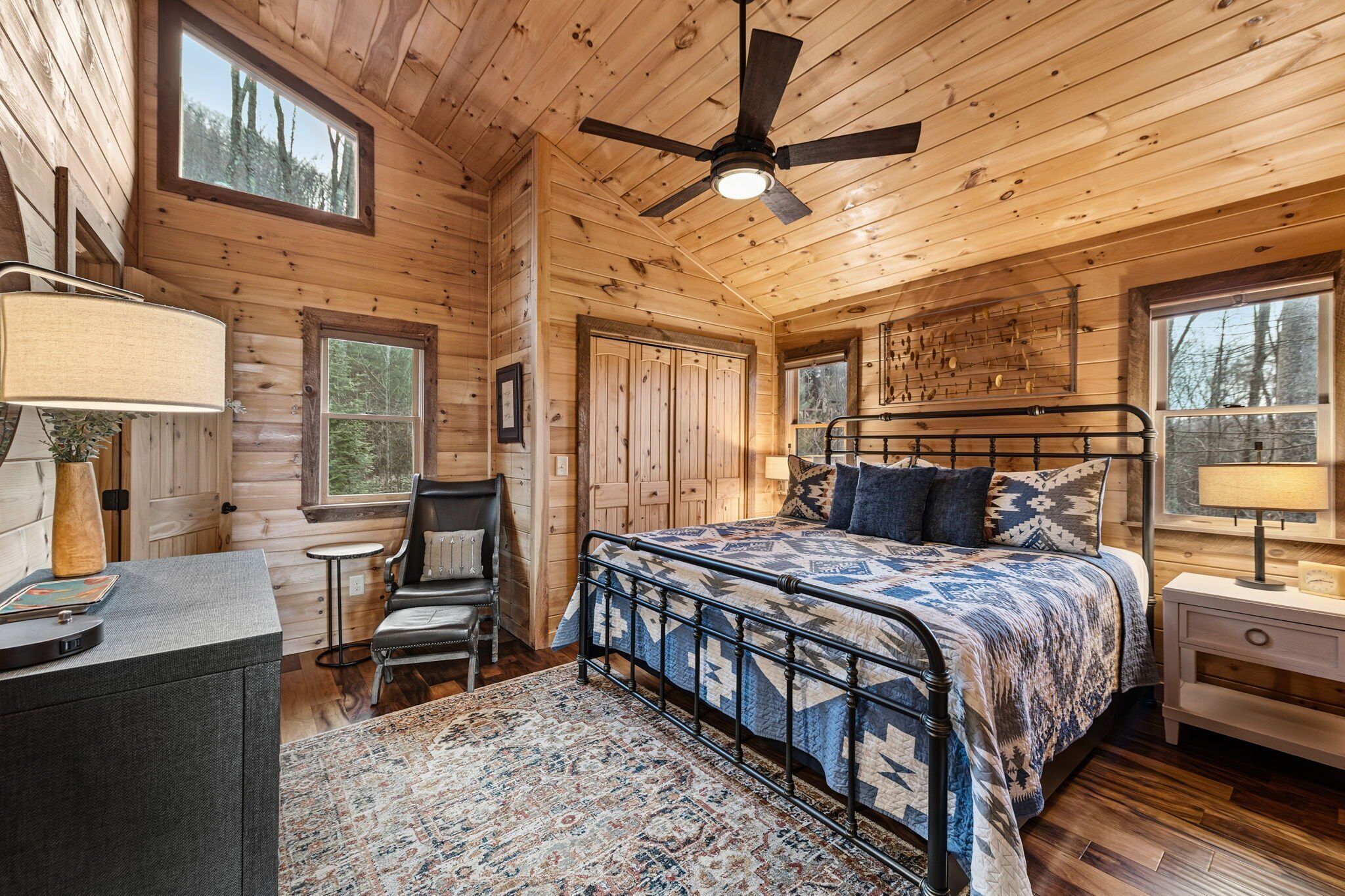A log cabin bedroom with a bed, a desk, a chair, and a ceiling fan.