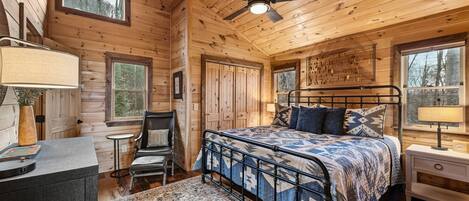 A log cabin bedroom with a bed, a desk, a chair, and a ceiling fan.