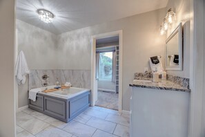 A modern bathroom with a marble vanity, a large bathtub, and a walk-in closet. - Year-Round Pool + Arcade + Claw Machine • Sleeps 14 • 10 Min to OU (Norman)