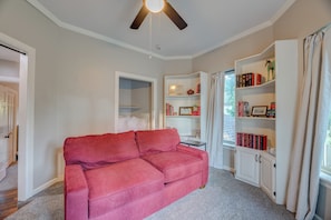 A living room with a red sofa, a ceiling fan, a bookshelf, and a window with curtains. - Year-Round Pool + Claw Machine Arcade • Sleeps 14 • Near OU (Norman)