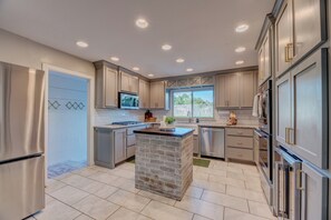 A modern kitchen with grey cabinets, a central island, stainless steel appliances, and a window providing natural light.