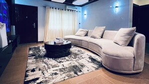A modern living room with a curved sofa, a coffee table, and a patterned rug. - Luxury 3-Bedroom Home in Maitama Abuja (Abuja)