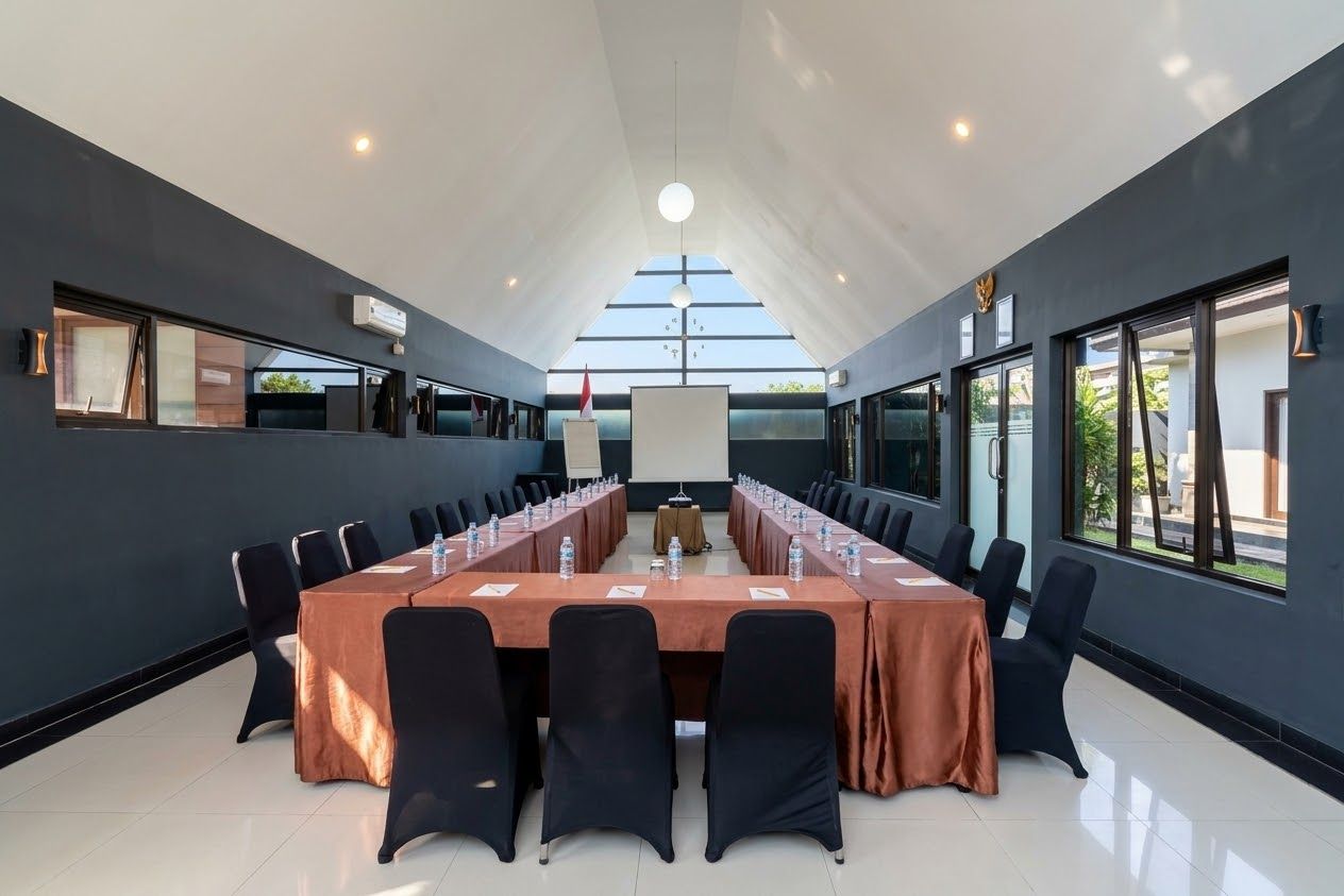 Un salón de conferencias con una larga mesa, sillas y una pantalla para proyector.