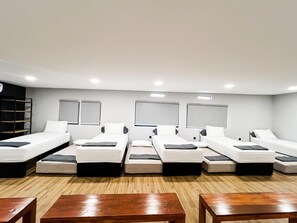A hotel room with six single beds arranged in a row, wooden flooring, and a small table in the foreground. - Oase Resort Bandung (Parongpong)