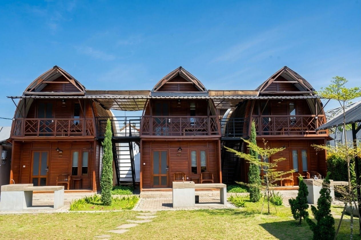 A row of wooden cabins with balconies, a covered walkway, and a small garden area.