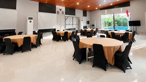 A conference room with multiple tables, black chairs, and a wooden ceiling with recessed lighting. - Oase Resort Bandung (Parongpong)